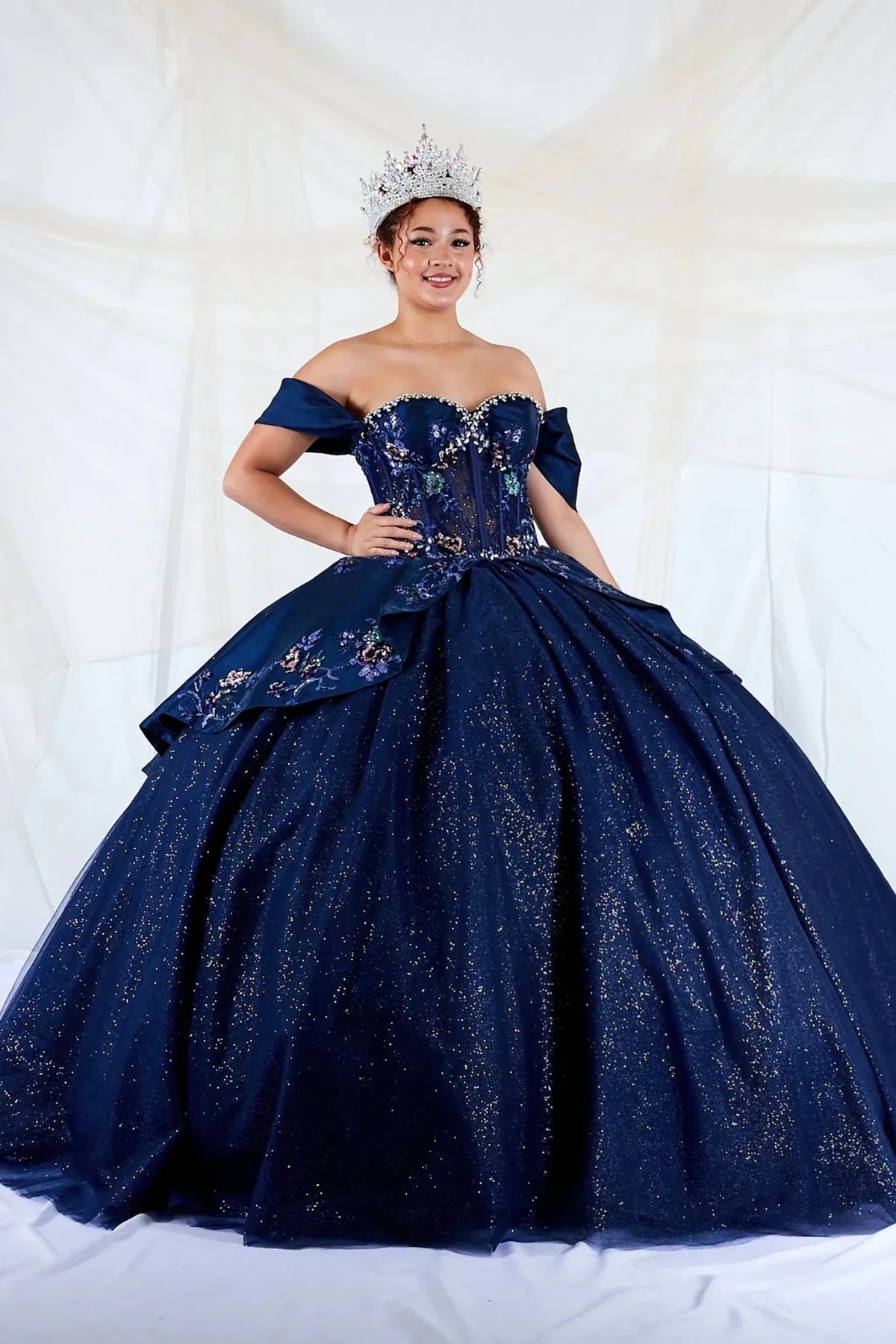 Navy quinceañera dress showcases jeweled satin bodice with embroidered peplum above glitter tulle skirt and lace-up back.