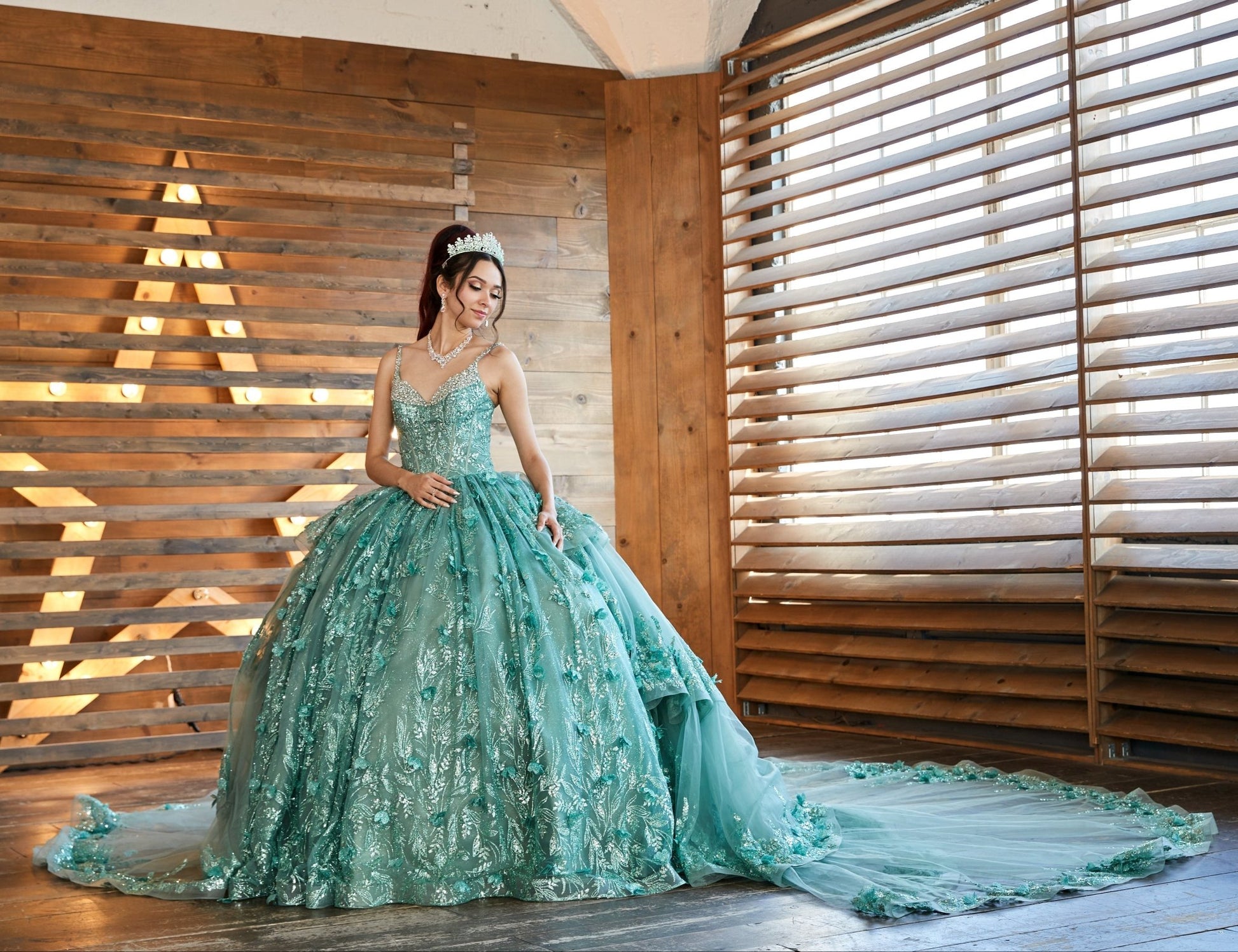 Front view of a woman wearing a sage quinceañera dress with sparkling glitter material and crystal accents