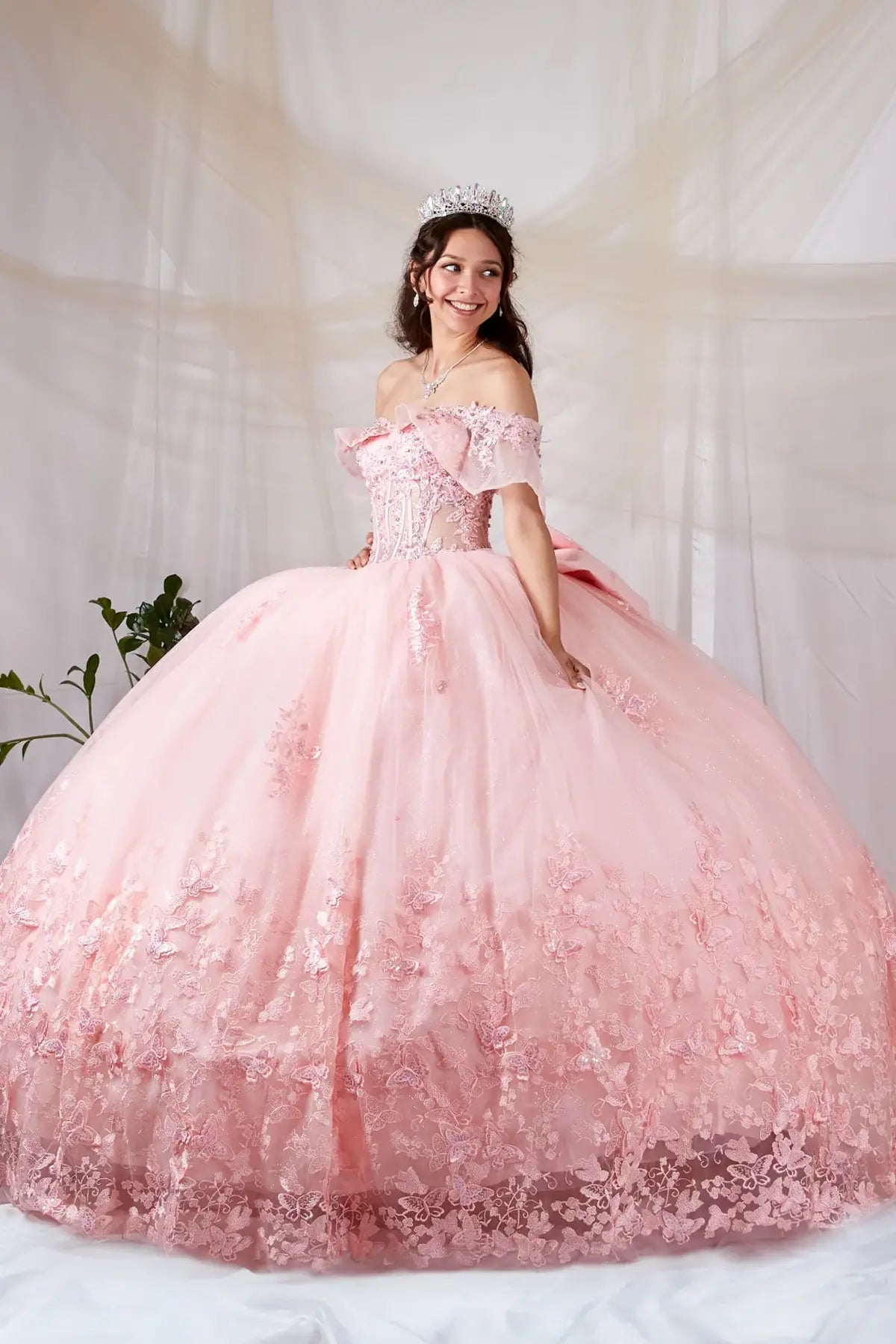 Side View of a woman wearing Soft pink gown with sheer bodice butterfly embellishments and layered airy skirt