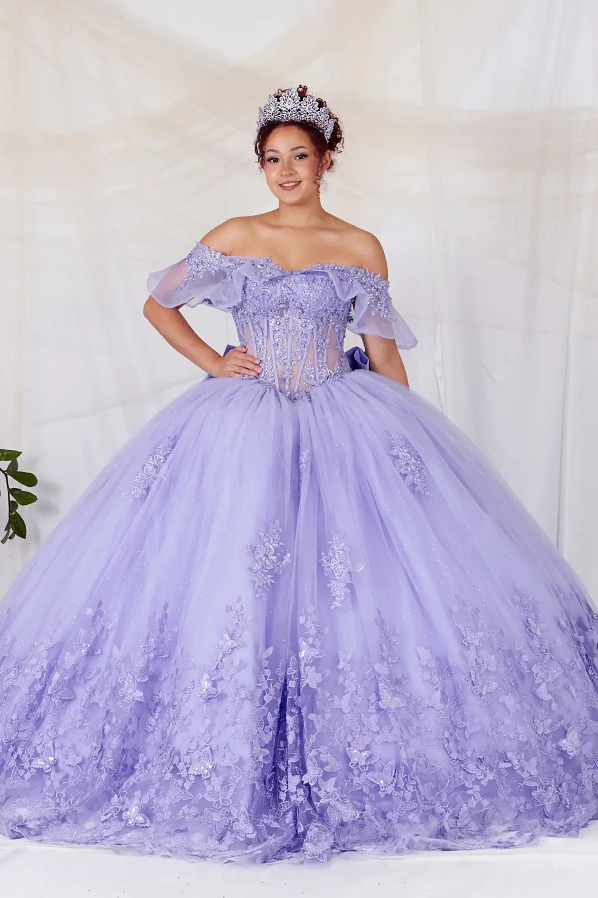 Front-Facing of a woman wearing Lilac ball gown with sheer off-shoulder flounce sleeves 3D butterfly accents and glitter tulle skirt for a statement quinceanera look