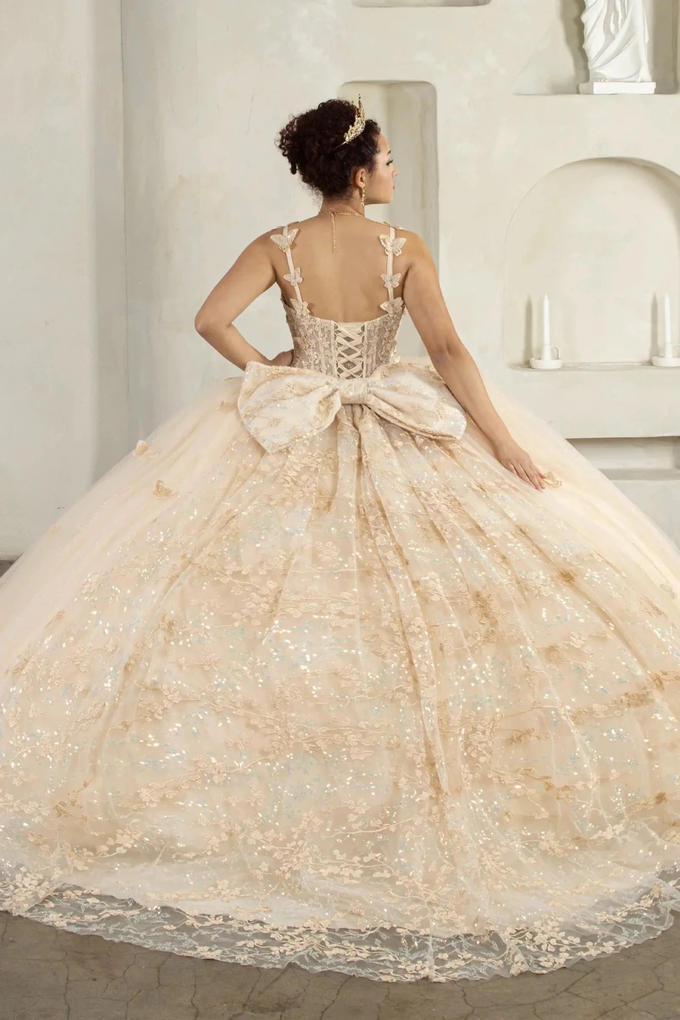 Back-Facing of a woman wearing Champagne formal gown featuring detachable bow accent layered skirt and flowing silhouette