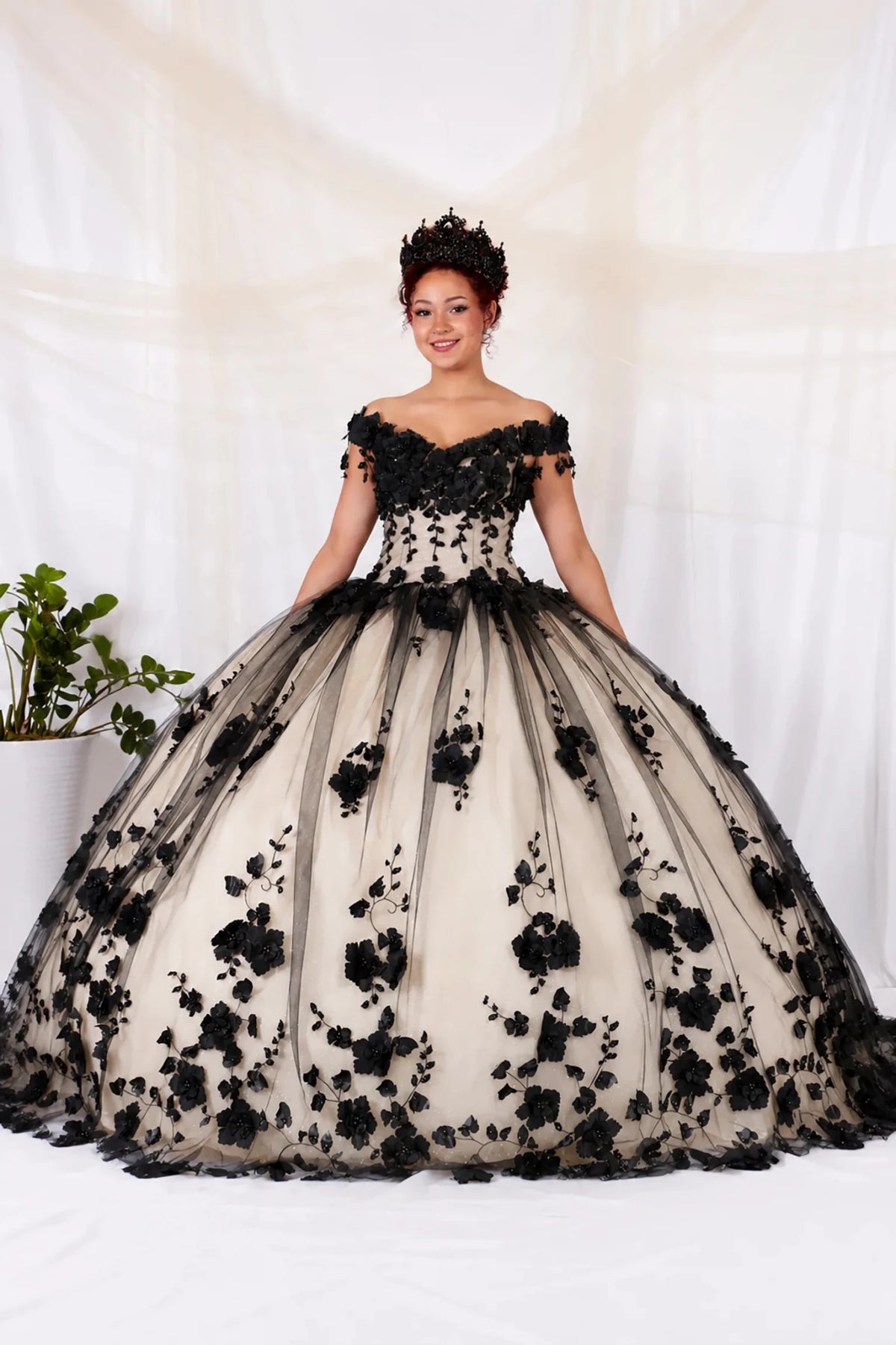 Black quinceañera ball gown with off‑shoulder neckline, 3D floral applique over beige tulle and layered train