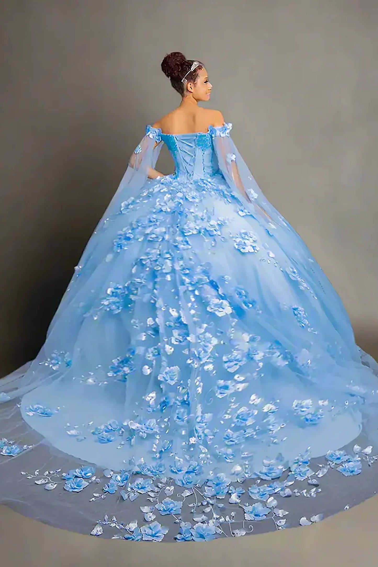 Back-Facing of a woman wearing Light blue quinceanera dress with 3d flowers, lace up back and detachable cape accent