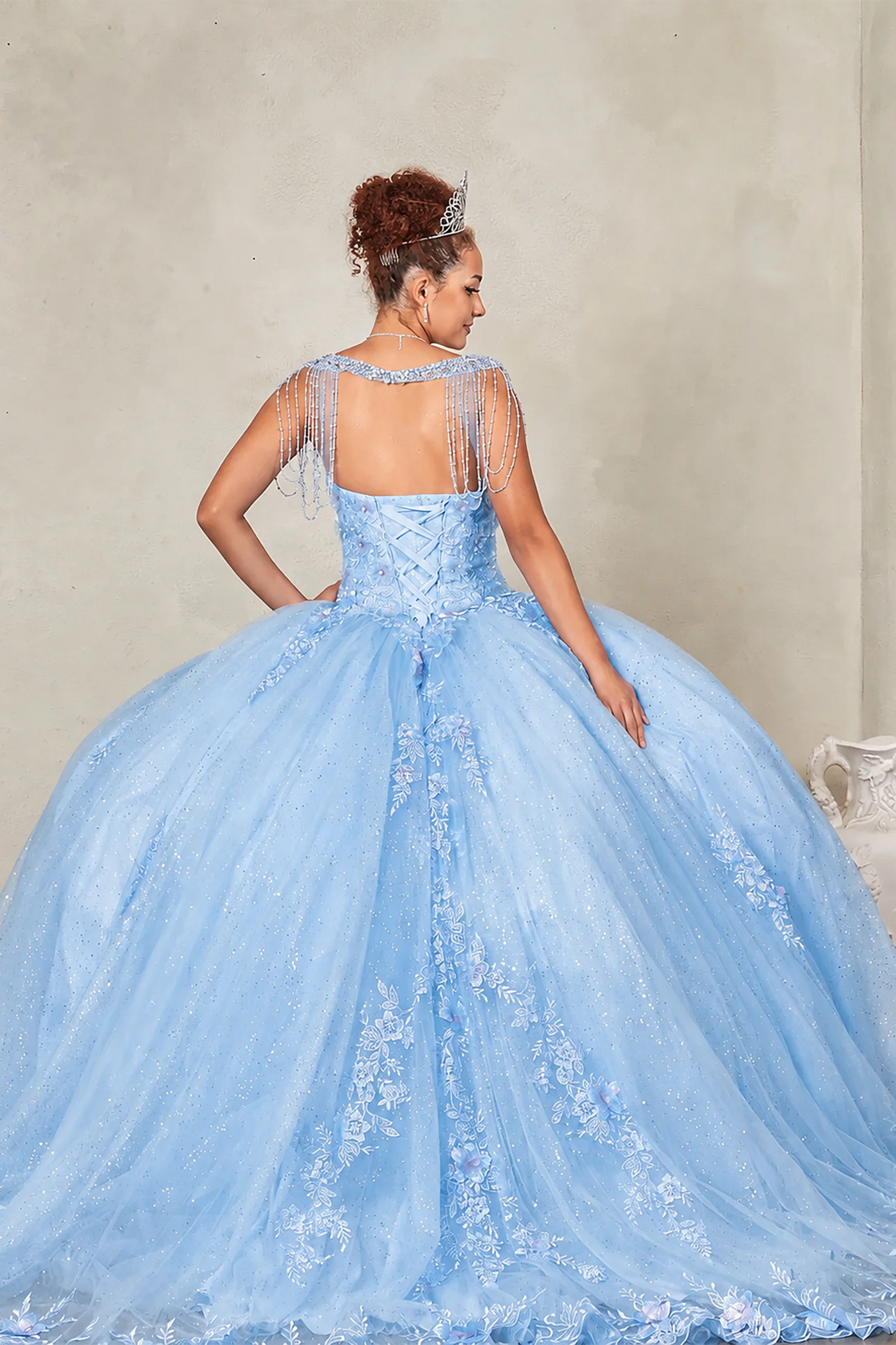 Blue quinceañera ball gown extending into graceful train with lace appliqués accenting bead-fringed