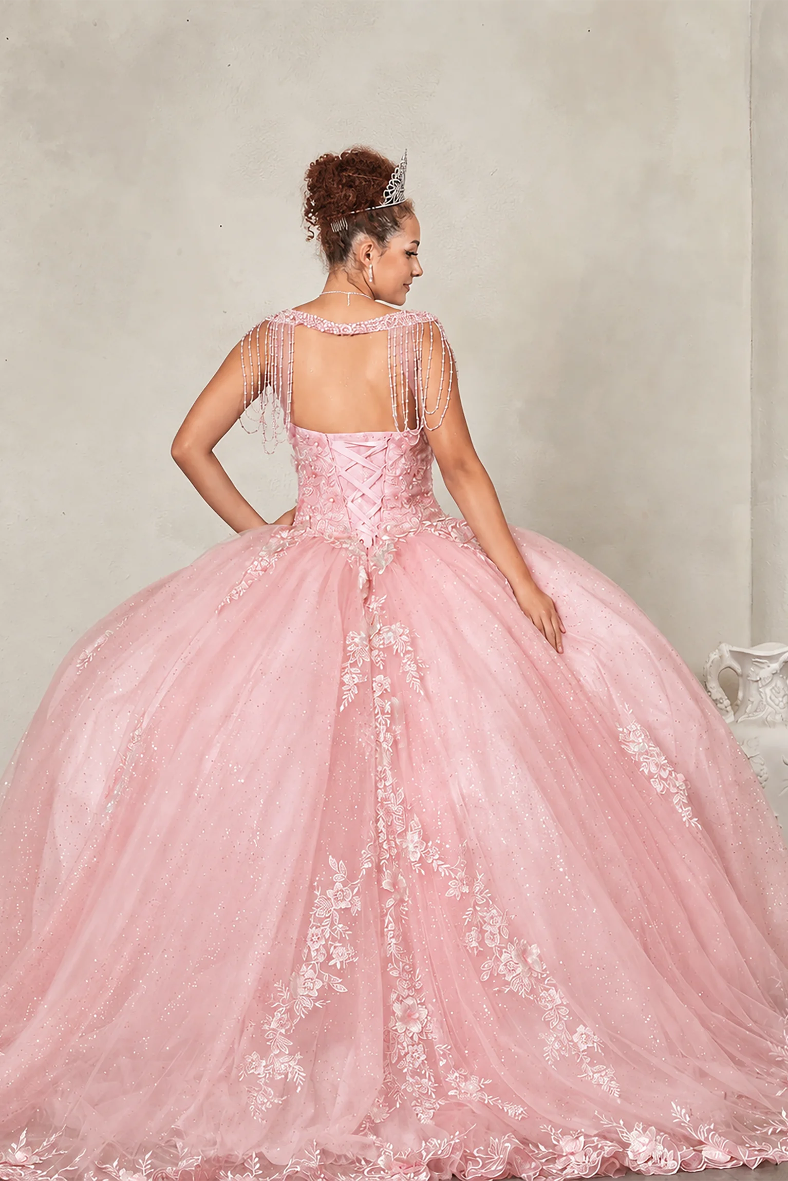 Blush quinceañera ball gown extending into graceful train with lace appliqués accenting bead-fringed