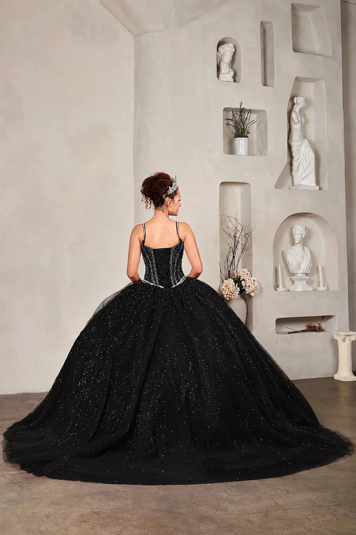 Black quinceañera ball gown with crystal beaded corset, V‑neckline, spaghetti straps and glitter tulle skirt