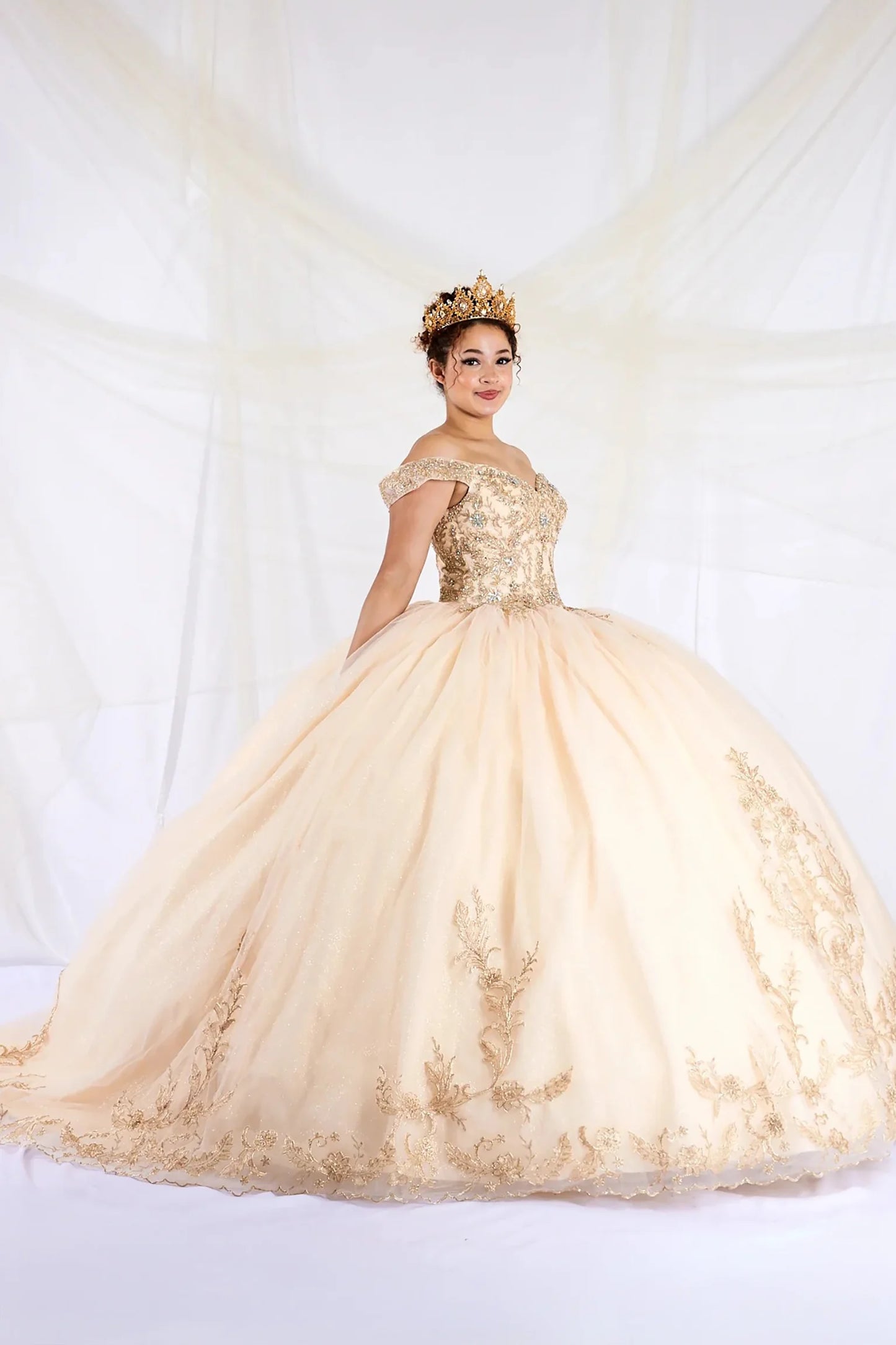 Front view of a woman wearing a champagne quinceañera dress with embroidered lace appliques, off-shoulder A-line silhouette and glitter tulle overlay