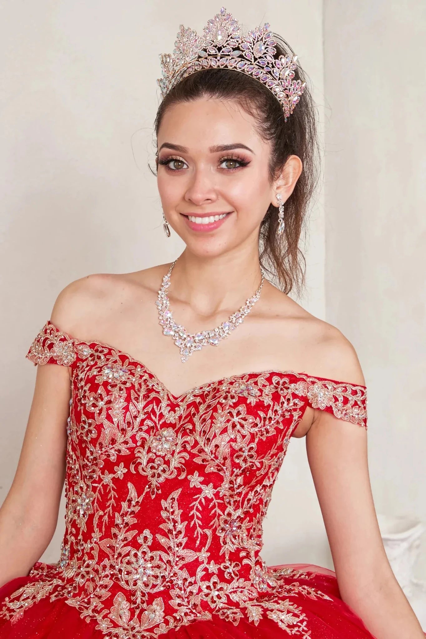 Red quinceañera ball gown with off‑shoulder neckline, gold embroidered lace applique and glitter tulle overlay