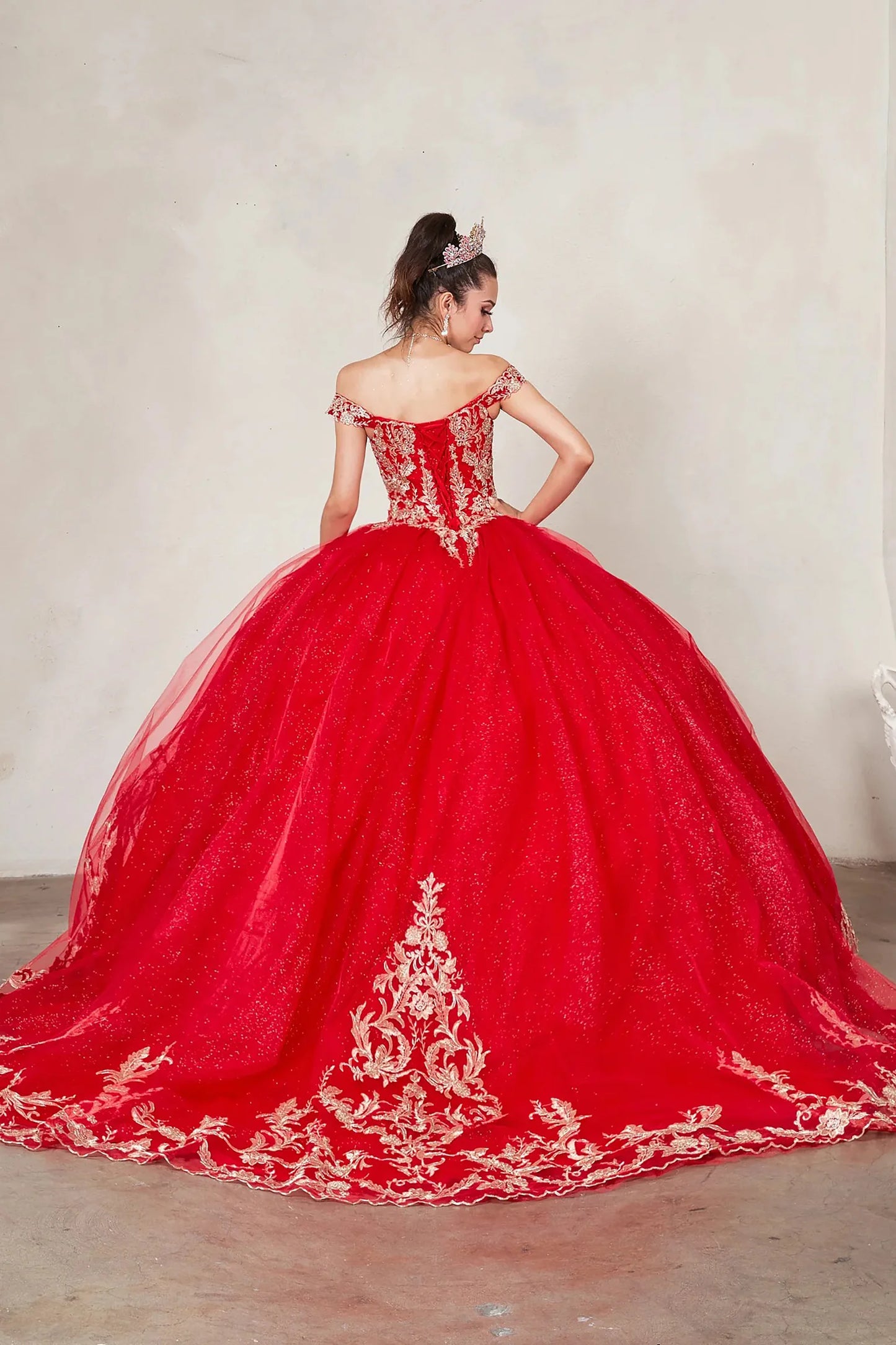 Back view of a woman wearing a red quinceañera dress with embroidered lace appliques, off-shoulder design and glitter tulle overlay
