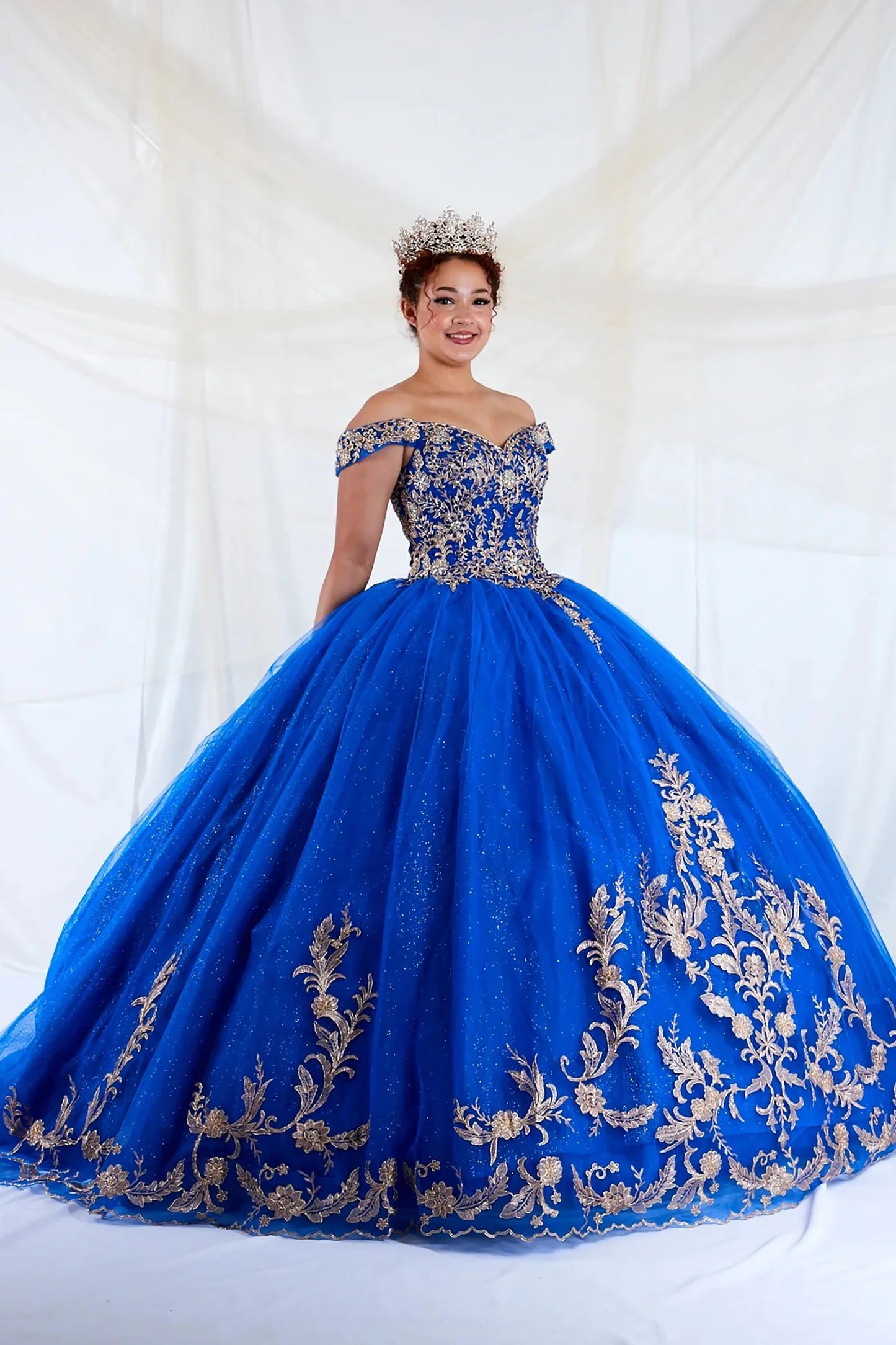 Front view of a woman wearing a royal blue quinceañera dress with embroidered lace appliques, off-shoulder A-line silhouette and glitter tulle overlay