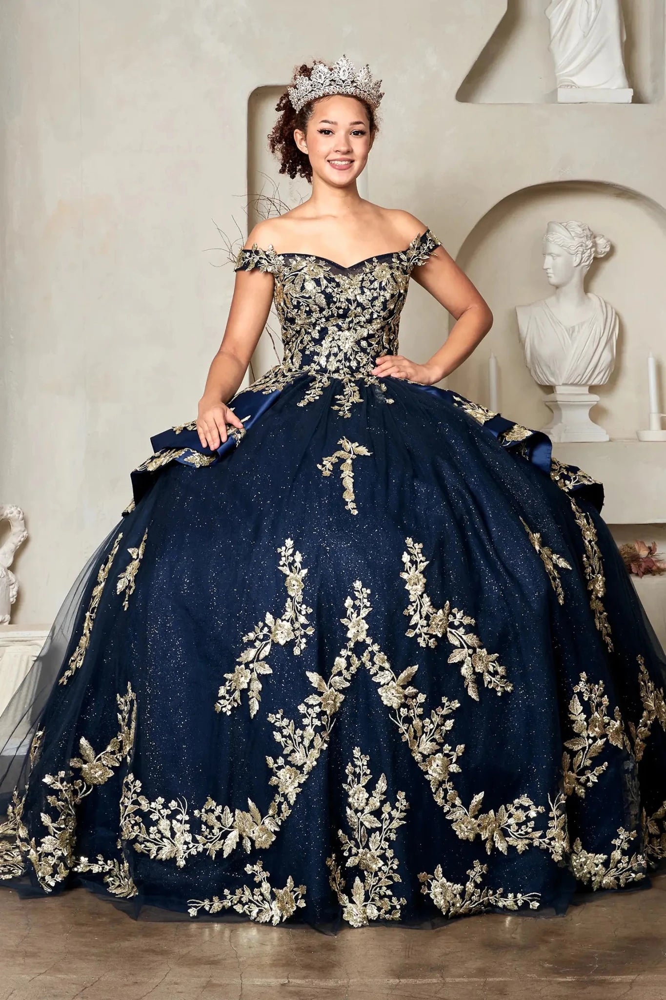 Navy quinceañera ball gown with off‑shoulder neckline, beaded gold embroidery and glitter layered skirt