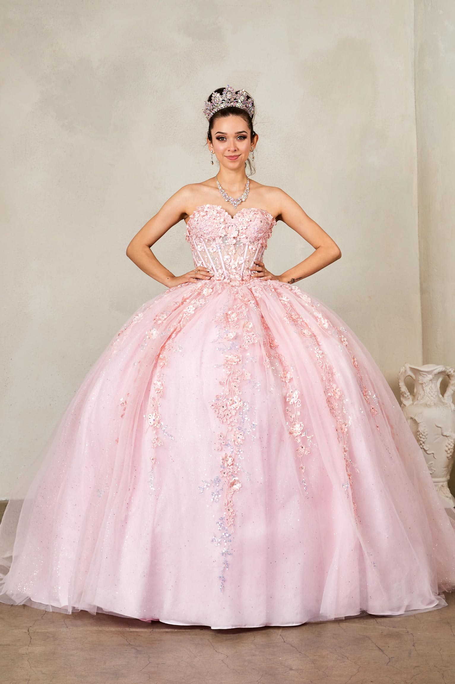 Front view of a woman wearing a blush quinceañera dress with glitter tulle and 3D floral flowers