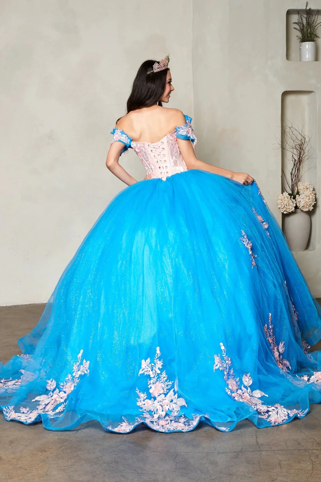 Turquoise quinceañera ball gown with off‑shoulder neckline, blush floral applique, crystal beaded bodice and glitter tulle skirt