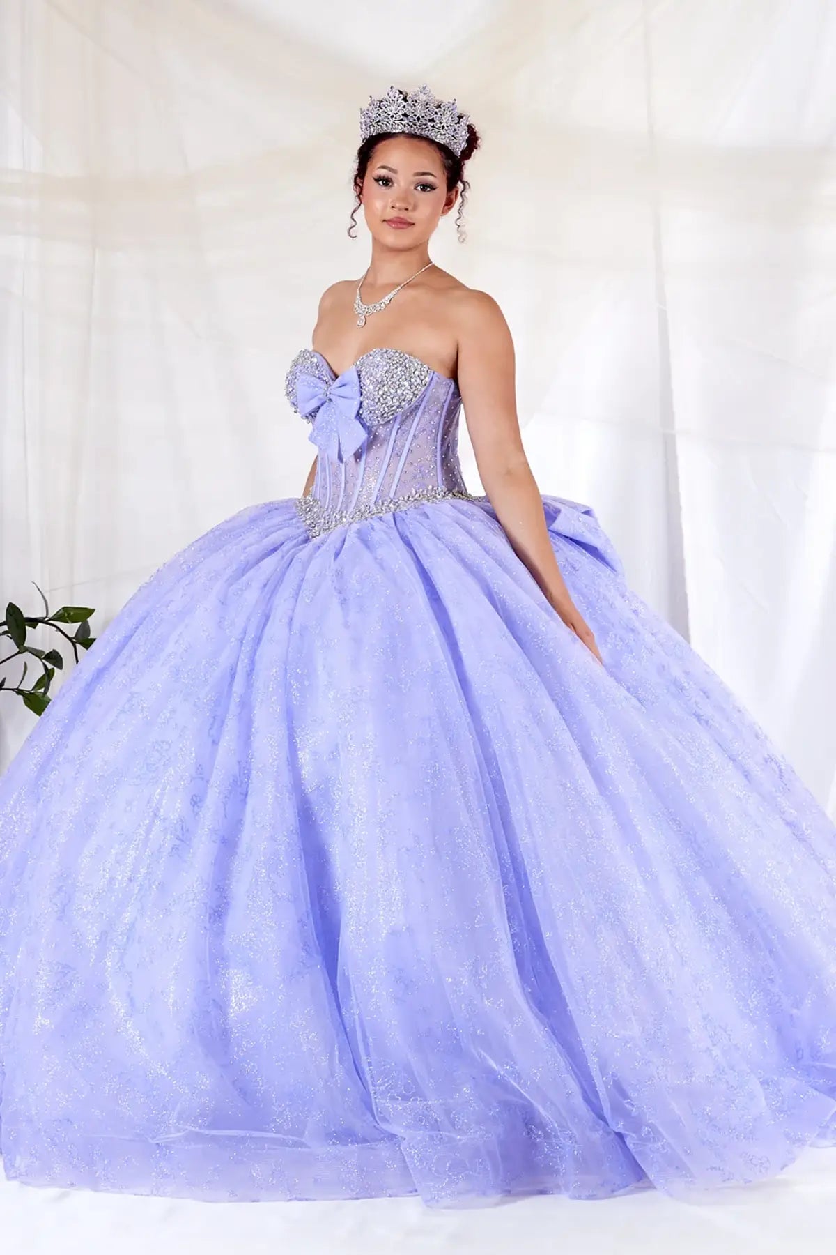 Lilac quinceañera ball gown with sheer corset bodice, crystal beading, glitter floral tulle and bow detail