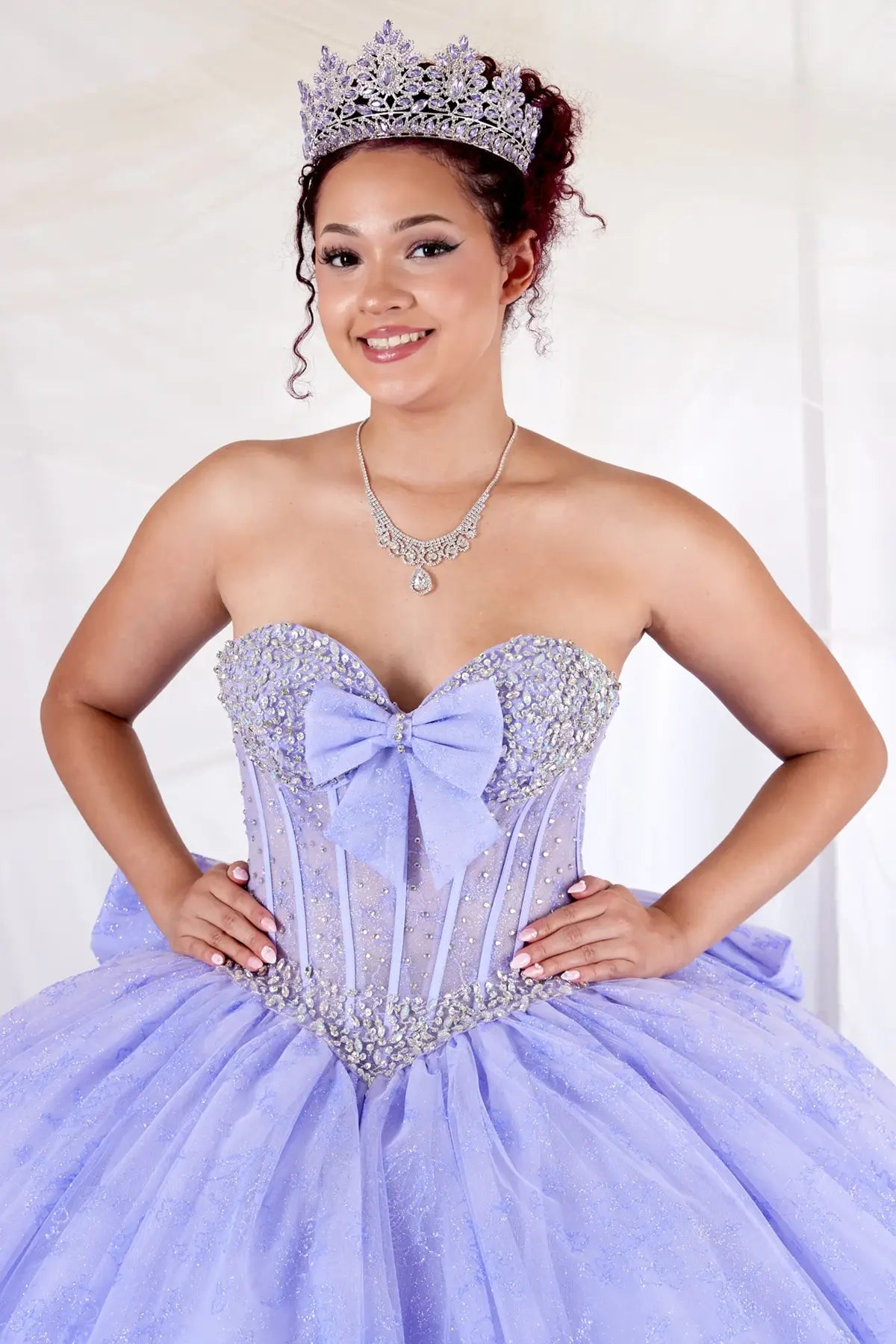 Lilac quinceañera ball gown with sheer corset bodice, crystal beading, glitter floral tulle and bow detail