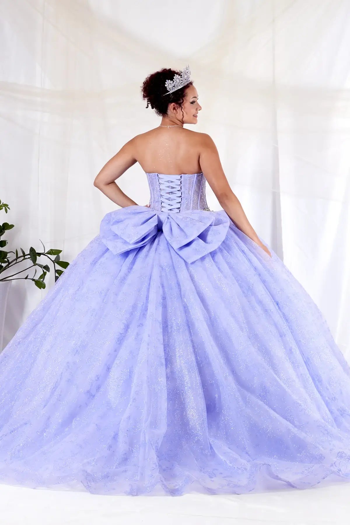 Lilac quinceañera ball gown with sheer corset bodice, crystal beading, glitter floral tulle and bow detail