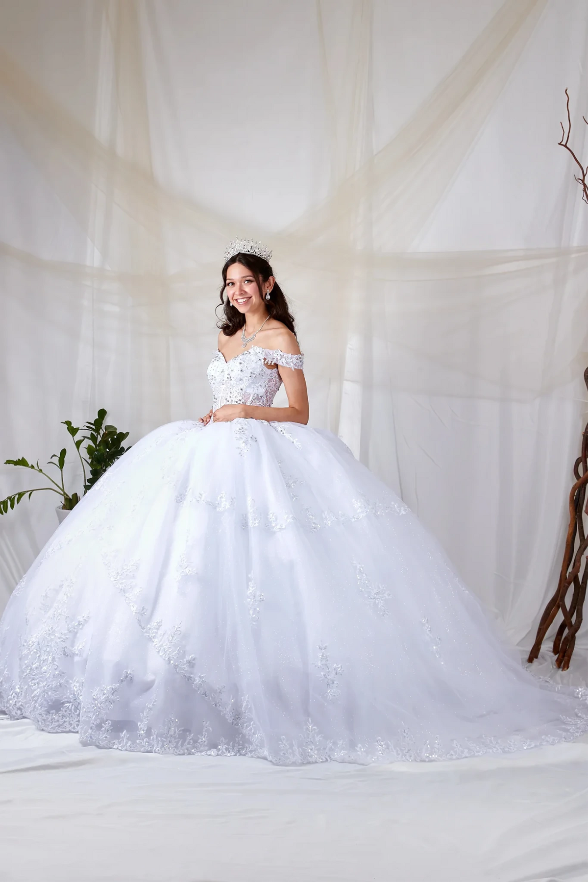 White quinceañera ball gown with off‑shoulder neckline, sheer sweetheart bodice, floral embroidery and glitter tulle skirt