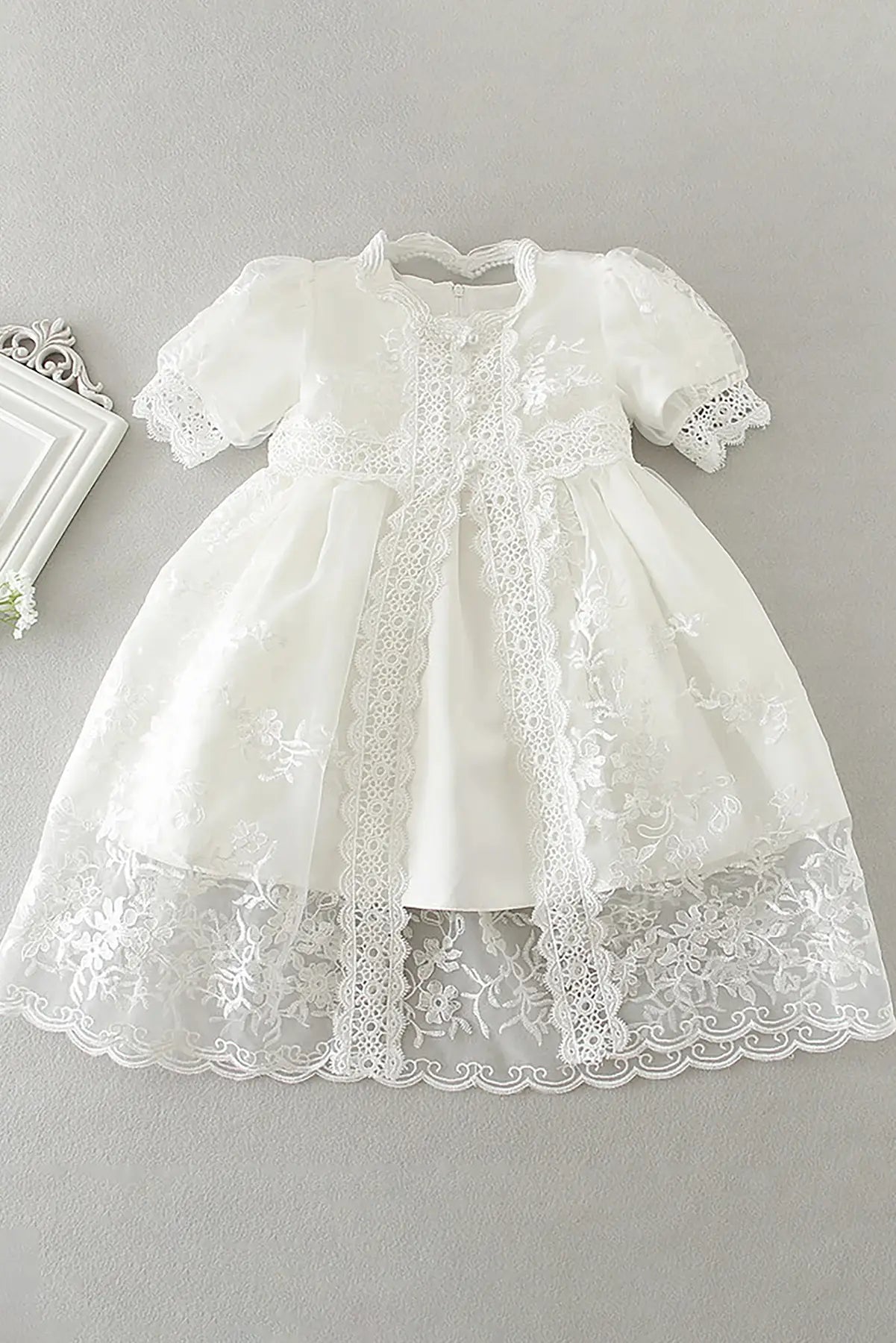 White lace baby cap sleeve dress on a gray background. 
