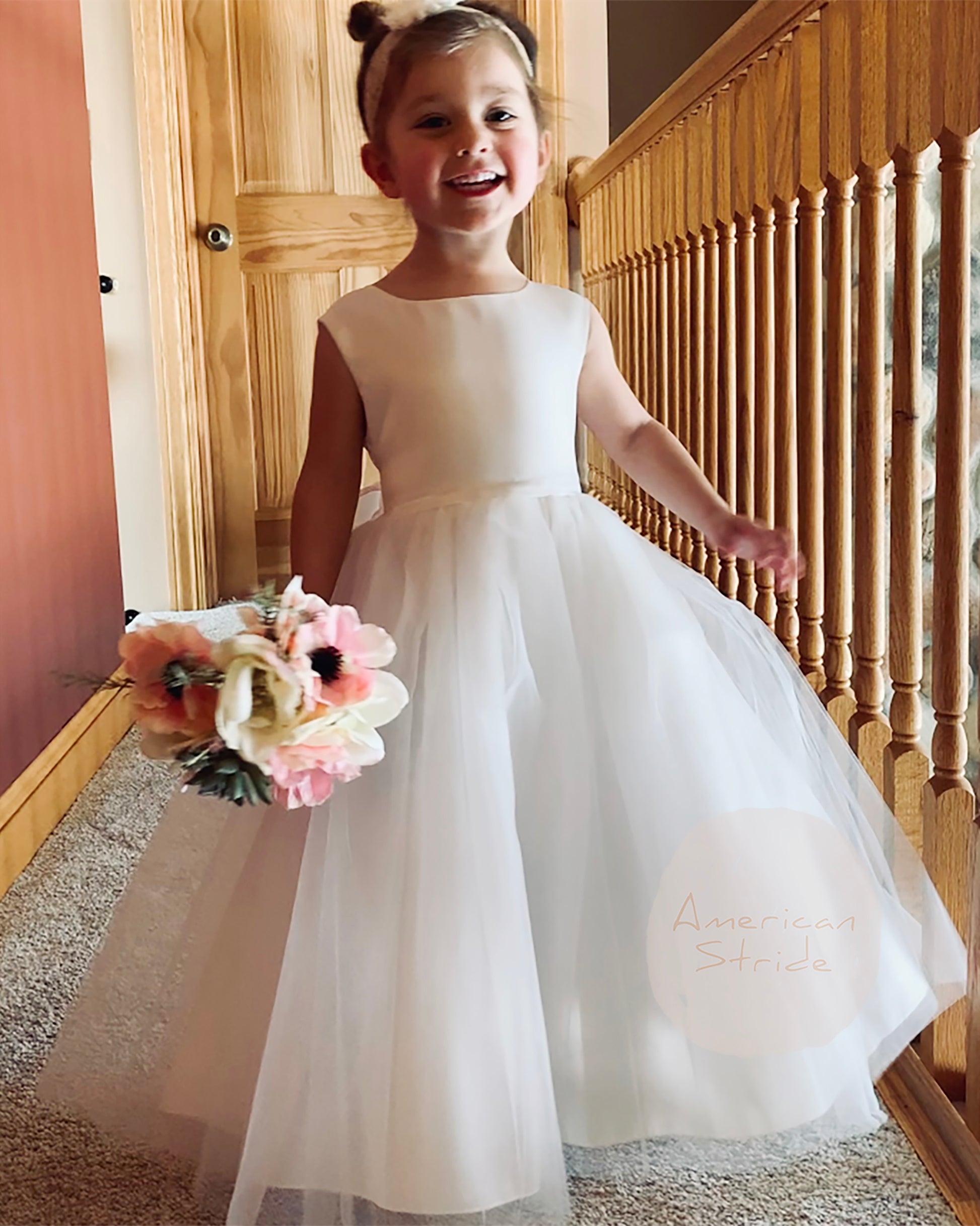Young girl in a white dress holding flowers indoors.