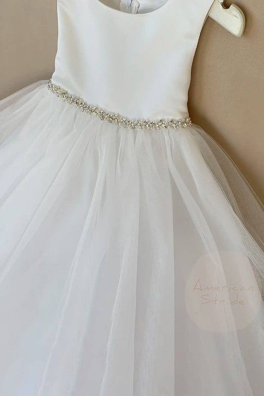 White flower girl dress with a beaded waistband on a beige background. the top is satin, and the skirt is 4 layer of tulles.