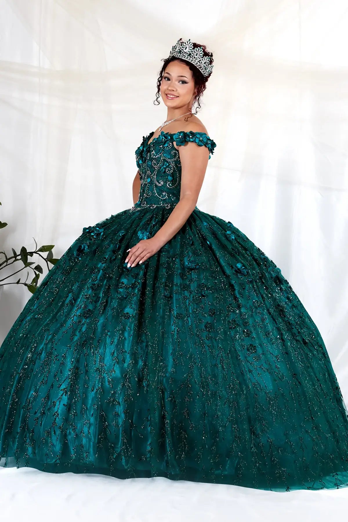 Side View of a woman wearing Rich green gown with dimensional floral accents off-shoulder styling and flowing silhouette