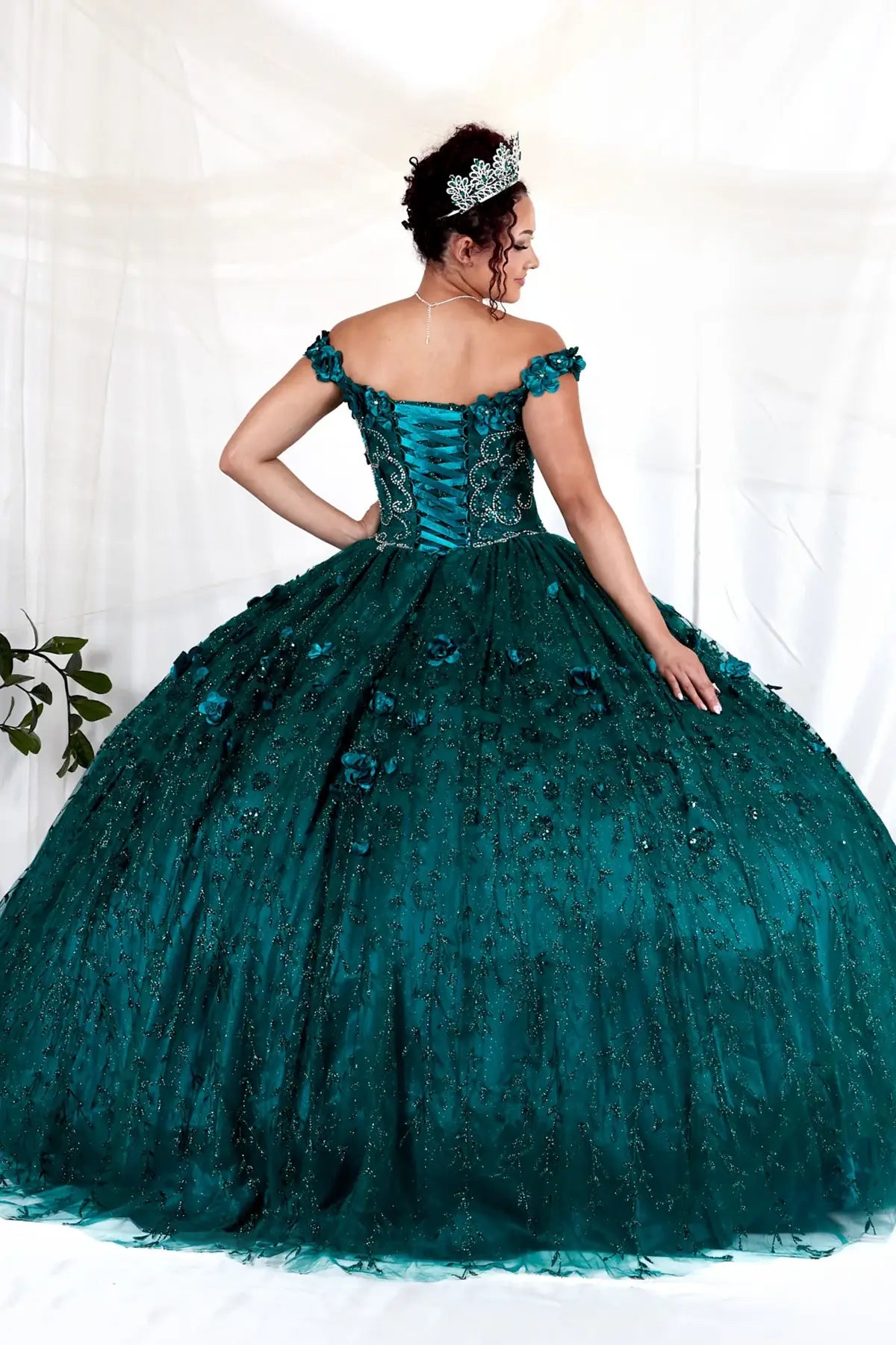 Back-Facing of a woman wearing Emerald formal gown featuring long trailing tail layered skirt and structured back design