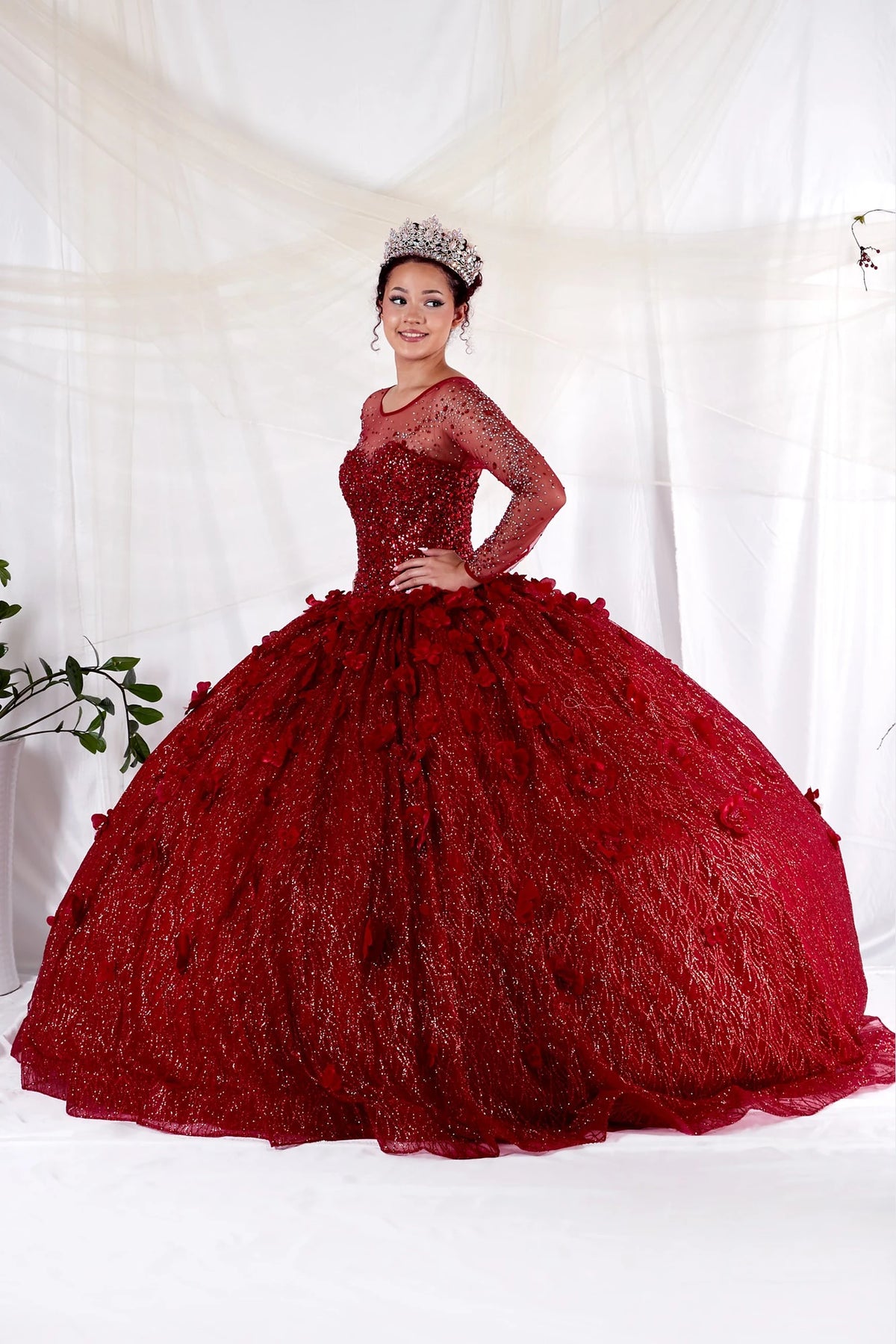 Burgundy quinceañera dress showcases sheer embellished long sleeves above textured lace ball gown skirt.