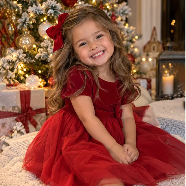 Girl in a red holiday dress beside a Christmas tree